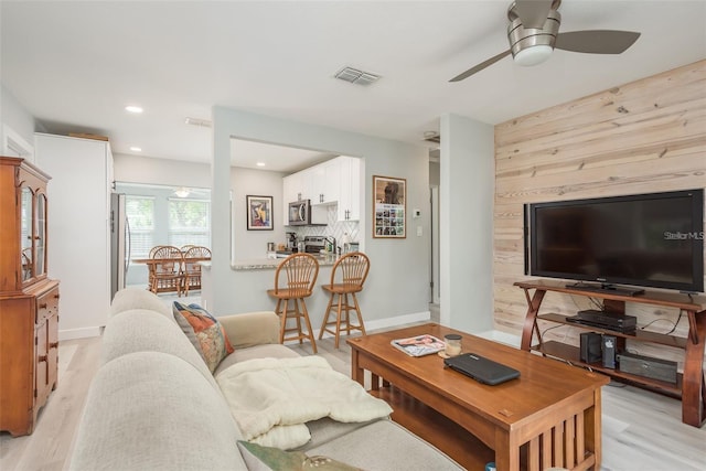 living room featuring light hardwood / wood-style floors, ceiling fan, and wooden walls