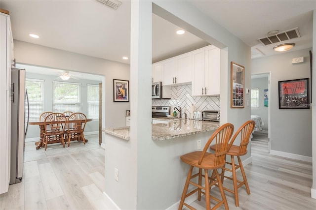 kitchen featuring backsplash, light stone counters, appliances with stainless steel finishes, a kitchen bar, and white cabinetry