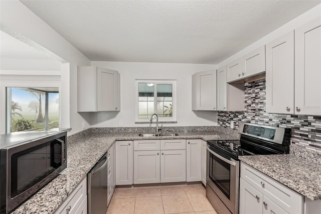 kitchen featuring white cabinets, sink, appliances with stainless steel finishes, light tile patterned flooring, and light stone counters