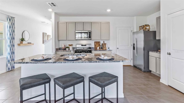 kitchen with gray cabinetry, stainless steel appliances, a kitchen island with sink, sink, and stone counters