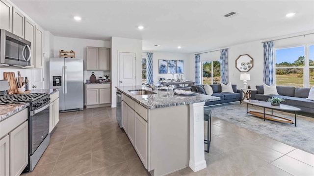 kitchen with sink, light tile patterned floors, a center island with sink, and appliances with stainless steel finishes