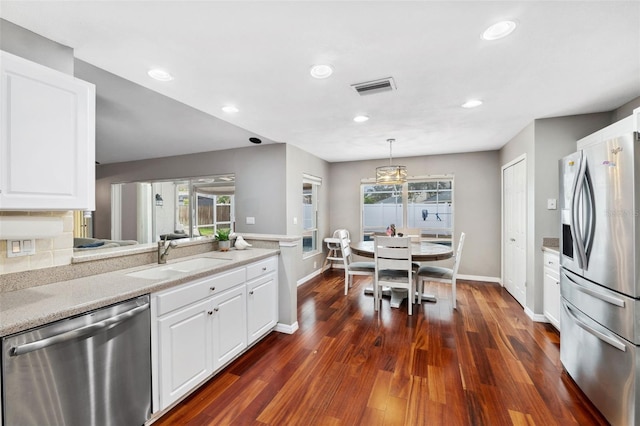 kitchen with light stone countertops, appliances with stainless steel finishes, sink, white cabinetry, and hanging light fixtures