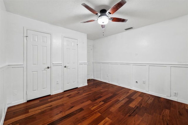 unfurnished bedroom with multiple closets, ceiling fan, and dark wood-type flooring