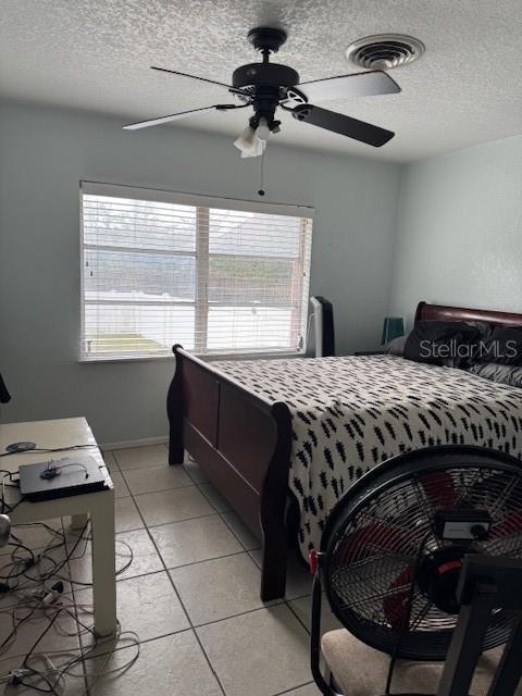 tiled bedroom featuring multiple windows, ceiling fan, and a textured ceiling