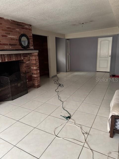 unfurnished living room featuring a fireplace, light tile patterned floors, and a textured ceiling