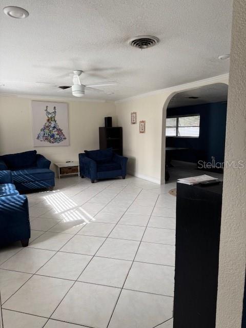 tiled living room with ceiling fan, a textured ceiling, and ornamental molding