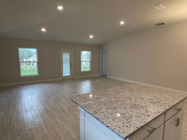 kitchen with light stone countertops, a center island, light hardwood / wood-style floors, vaulted ceiling, and white cabinets