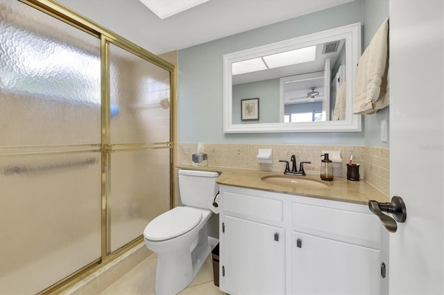 bathroom with tile patterned floors, toilet, vanity, a shower with shower door, and tile walls