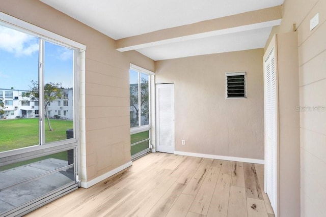 spare room featuring light hardwood / wood-style floors and beam ceiling