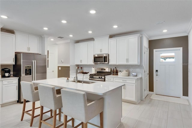 kitchen with appliances with stainless steel finishes, white cabinetry, a kitchen island with sink, and sink