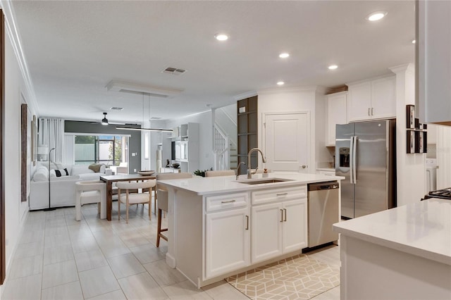 kitchen with stainless steel appliances, ceiling fan, sink, white cabinets, and an island with sink