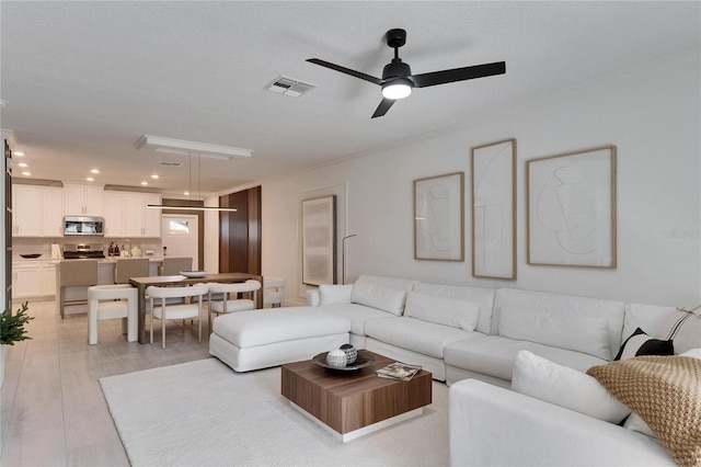 living room featuring ceiling fan, crown molding, and light wood-type flooring