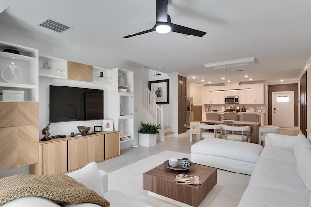 living room featuring ceiling fan, built in features, light wood-type flooring, and ornamental molding