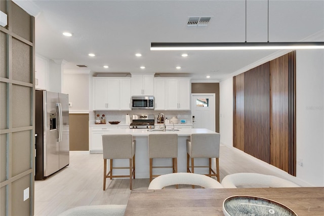 kitchen featuring a kitchen breakfast bar, white cabinetry, a kitchen island with sink, and appliances with stainless steel finishes