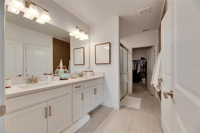 bathroom with vanity, a textured ceiling, and a shower with shower door