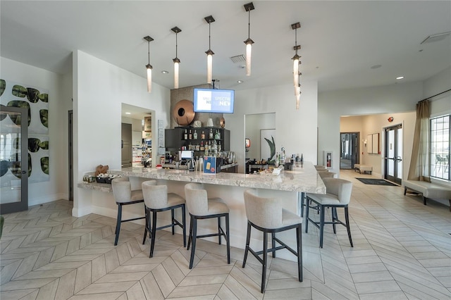 kitchen with a breakfast bar, light parquet floors, hanging light fixtures, light stone counters, and kitchen peninsula