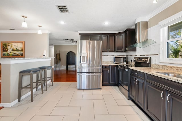 kitchen with pendant lighting, crown molding, wall chimney exhaust hood, appliances with stainless steel finishes, and tasteful backsplash