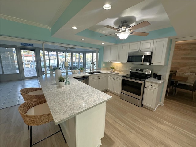 kitchen with decorative backsplash, stainless steel appliances, sink, white cabinets, and a breakfast bar area