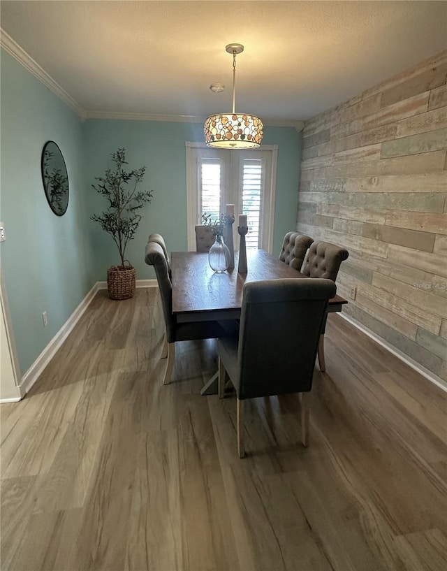 dining area featuring wood walls, wood-type flooring, and ornamental molding