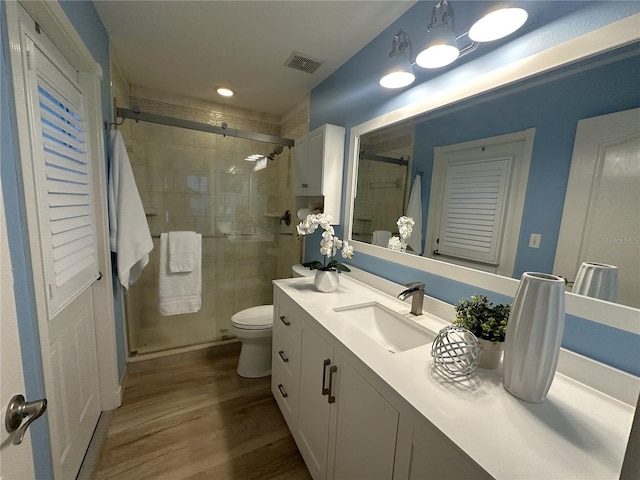 bathroom with a shower with door, vanity, wood-type flooring, and toilet