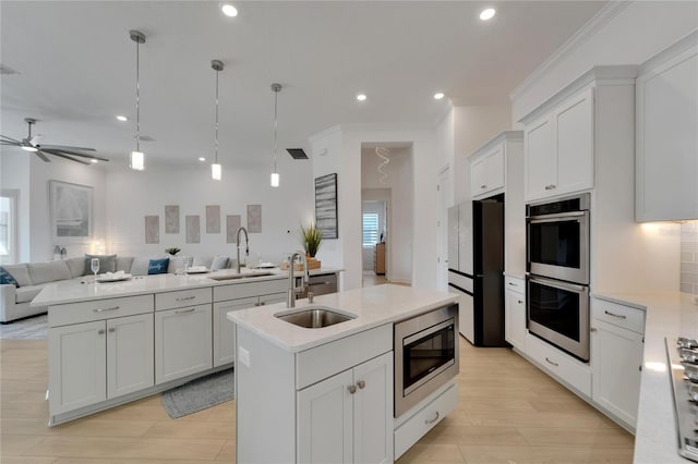 kitchen featuring a center island with sink, sink, hanging light fixtures, white cabinetry, and stainless steel appliances