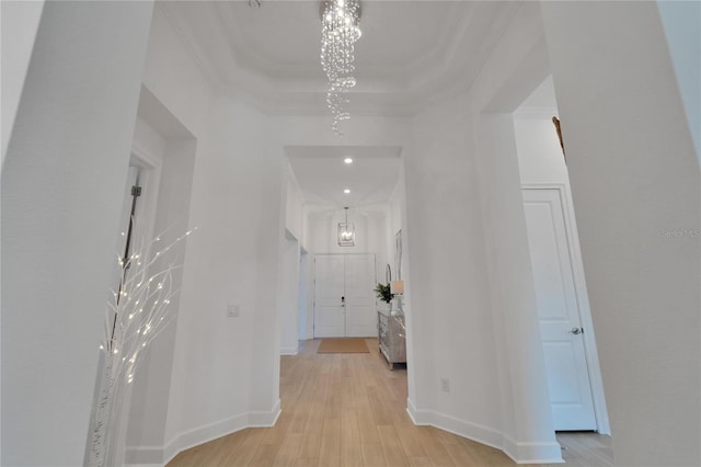 hall with light wood-type flooring, a raised ceiling, crown molding, and a notable chandelier