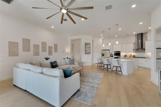 living room with light wood-type flooring, ceiling fan, and ornamental molding