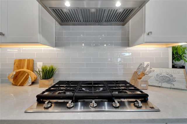 interior space with white cabinets, decorative backsplash, stainless steel gas cooktop, and wall chimney exhaust hood