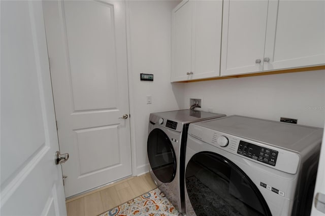 clothes washing area featuring cabinets, light hardwood / wood-style flooring, and washing machine and clothes dryer