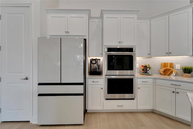 kitchen featuring freestanding refrigerator, double oven, white cabinets, tasteful backsplash, and light wood finished floors