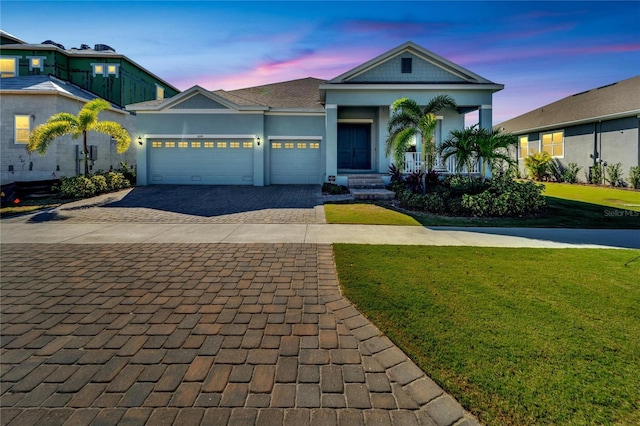 view of front facade featuring a yard, decorative driveway, covered porch, an attached garage, and stucco siding