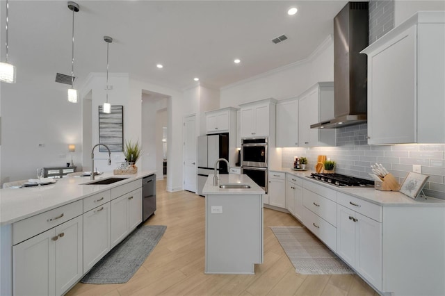kitchen with a sink, wall chimney exhaust hood, a kitchen island with sink, stainless steel appliances, and crown molding