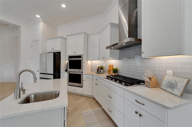 kitchen featuring appliances with stainless steel finishes, wall chimney exhaust hood, a sink, crown molding, and backsplash