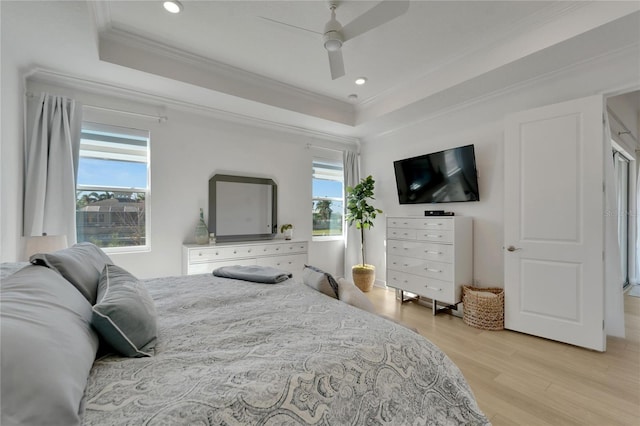 bedroom featuring multiple windows, light wood-style flooring, a tray ceiling, crown molding, and ceiling fan