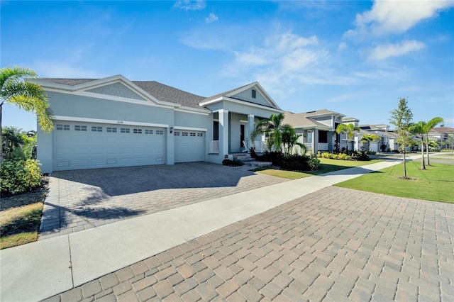 ranch-style home featuring decorative driveway, a garage, a front lawn, stucco siding, and a residential view