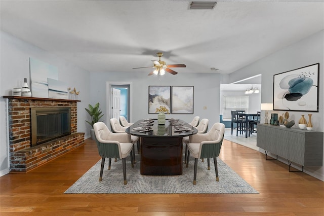 dining area featuring a brick fireplace, hardwood / wood-style floors, and ceiling fan with notable chandelier