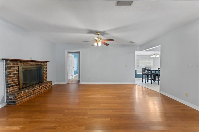 unfurnished living room featuring a brick fireplace, ceiling fan with notable chandelier, and hardwood / wood-style floors