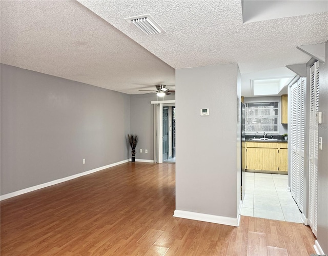 interior space featuring ceiling fan, sink, light hardwood / wood-style floors, and a textured ceiling