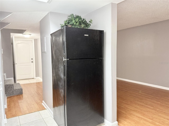 kitchen with black refrigerator, light tile patterned flooring, and a textured ceiling