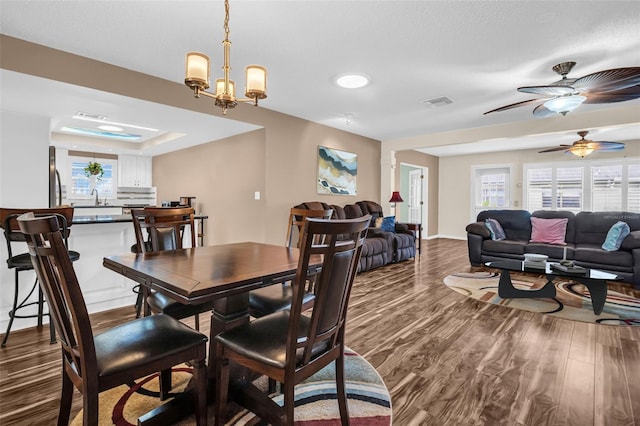 dining space featuring wood-type flooring, sink, and ceiling fan with notable chandelier