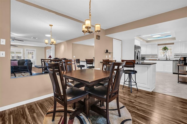 dining room featuring ceiling fan with notable chandelier, sink, light hardwood / wood-style flooring, and a raised ceiling