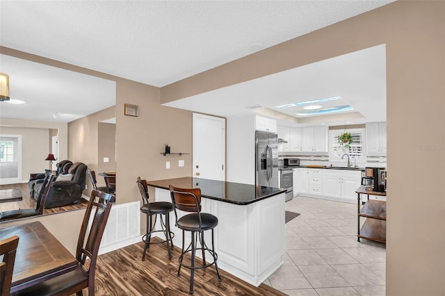 kitchen featuring kitchen peninsula, sink, a kitchen breakfast bar, stainless steel appliances, and white cabinets