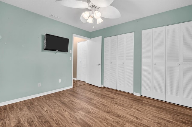 unfurnished bedroom featuring ceiling fan, hardwood / wood-style flooring, and multiple closets