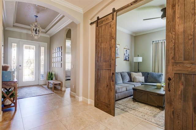 entryway featuring ceiling fan with notable chandelier, a barn door, ornamental molding, and light tile patterned floors