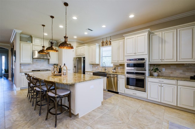 kitchen featuring light stone countertops, appliances with stainless steel finishes, pendant lighting, an island with sink, and range hood