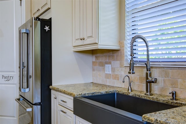 kitchen with backsplash, white cabinets, sink, high end fridge, and light stone counters