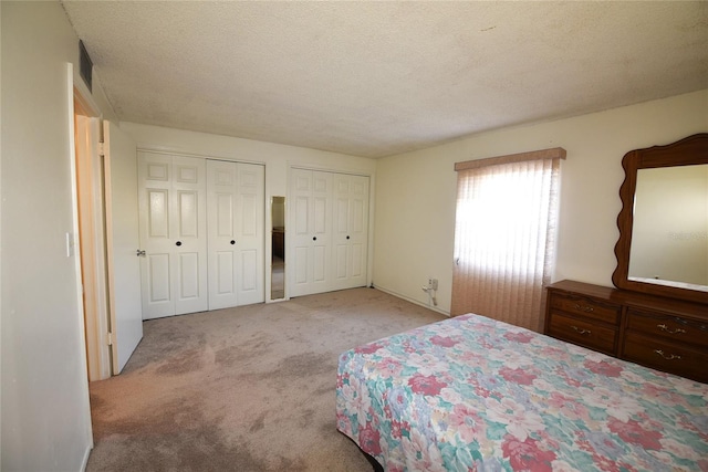 bedroom featuring two closets, light colored carpet, and a textured ceiling