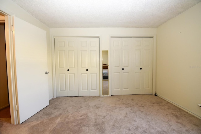 unfurnished bedroom featuring multiple closets, light carpet, and a textured ceiling