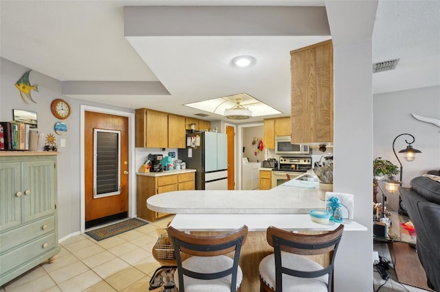 kitchen featuring sink, independent washer and dryer, light tile patterned flooring, kitchen peninsula, and stainless steel appliances