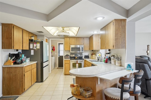 kitchen featuring sink, tasteful backsplash, kitchen peninsula, light tile patterned floors, and appliances with stainless steel finishes